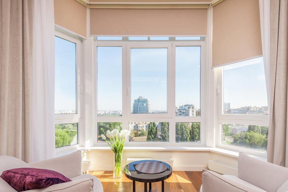 A bay window with tan curtains & window shades